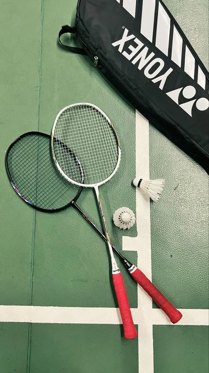 Perlengkapan badminton: raket, shuttlecock, dan tas Yonex di atas lapangan